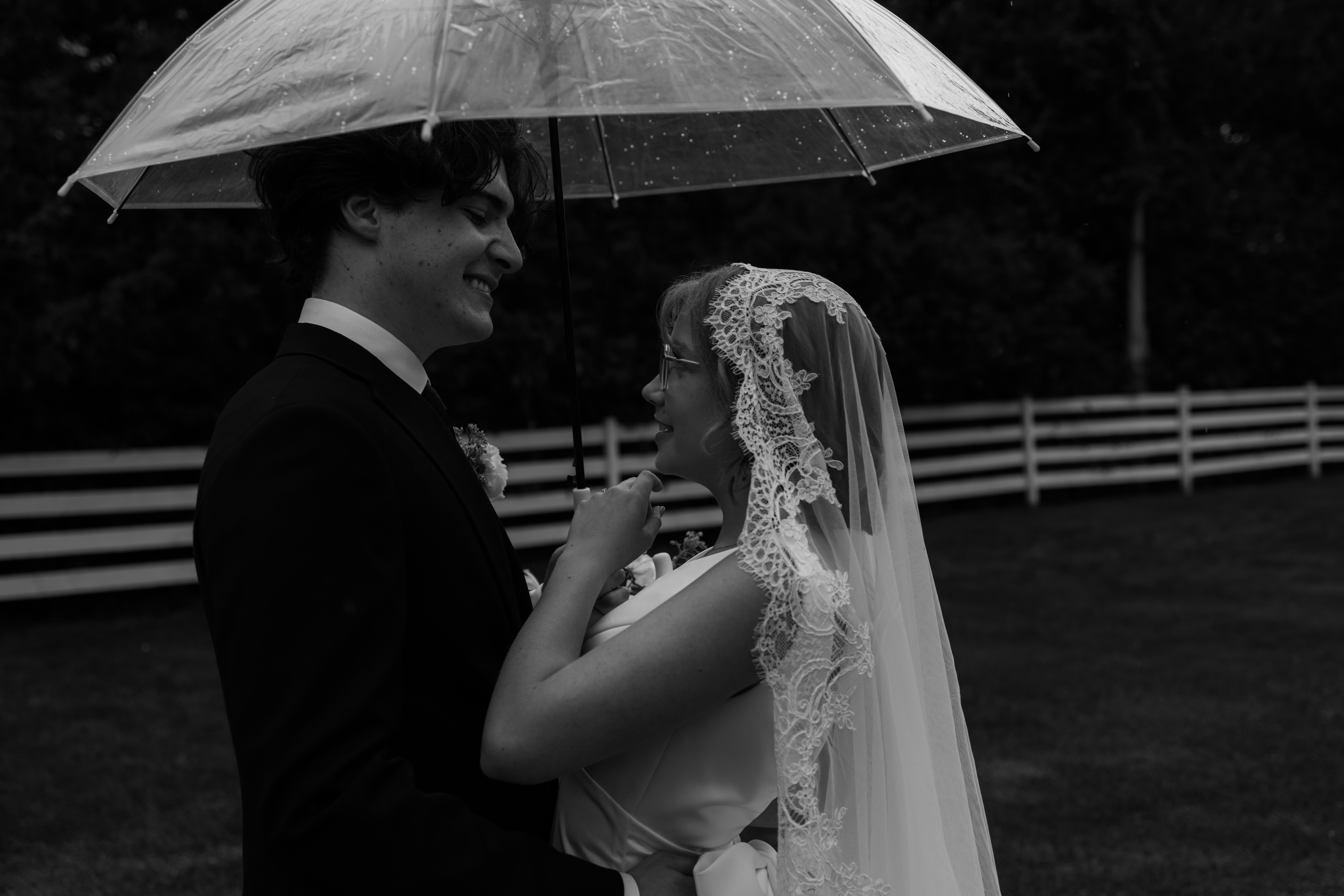 bride and groom share a moment under umbrella during rain on wedding day