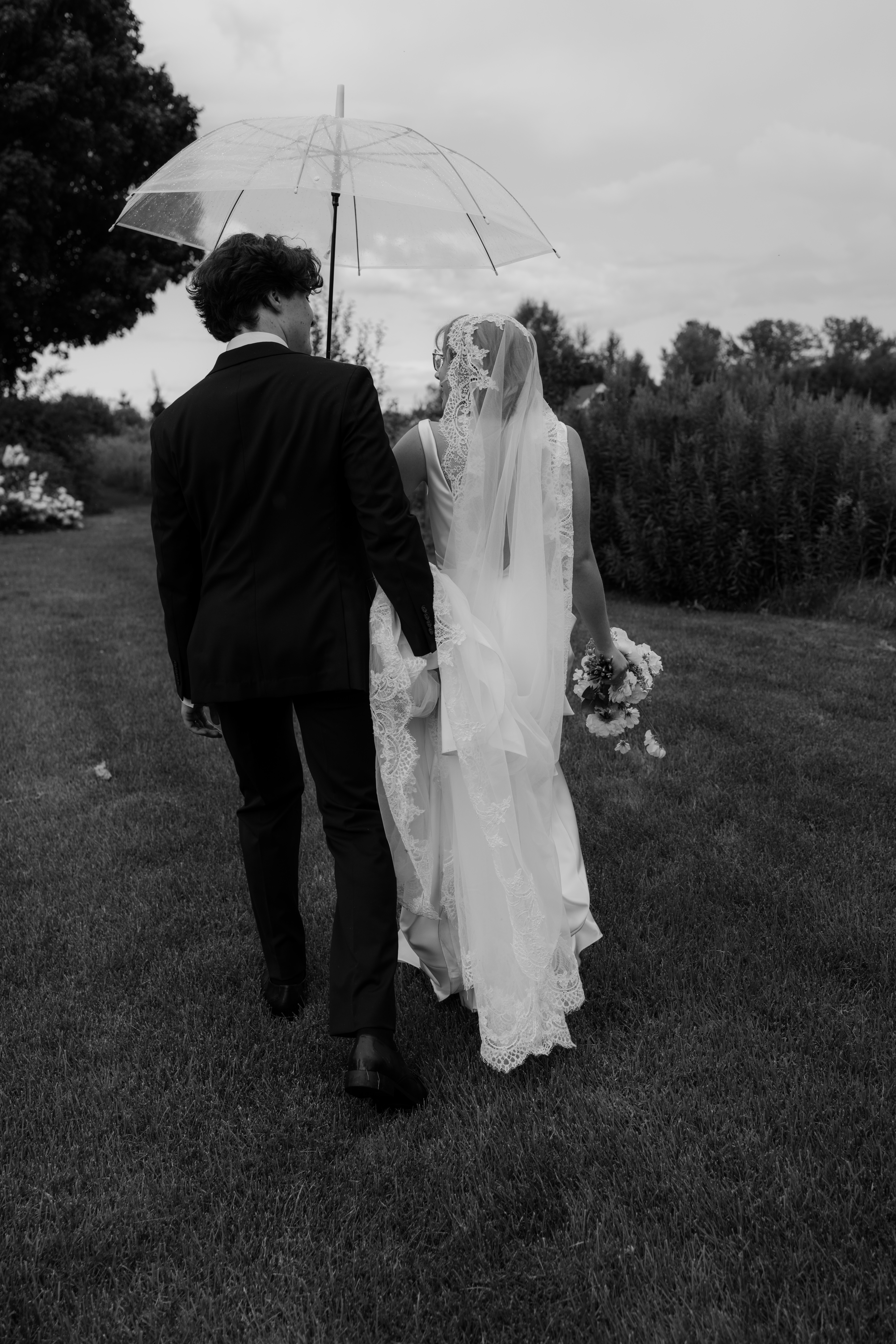 stylish bride and groom walking in the rain under umbrella 