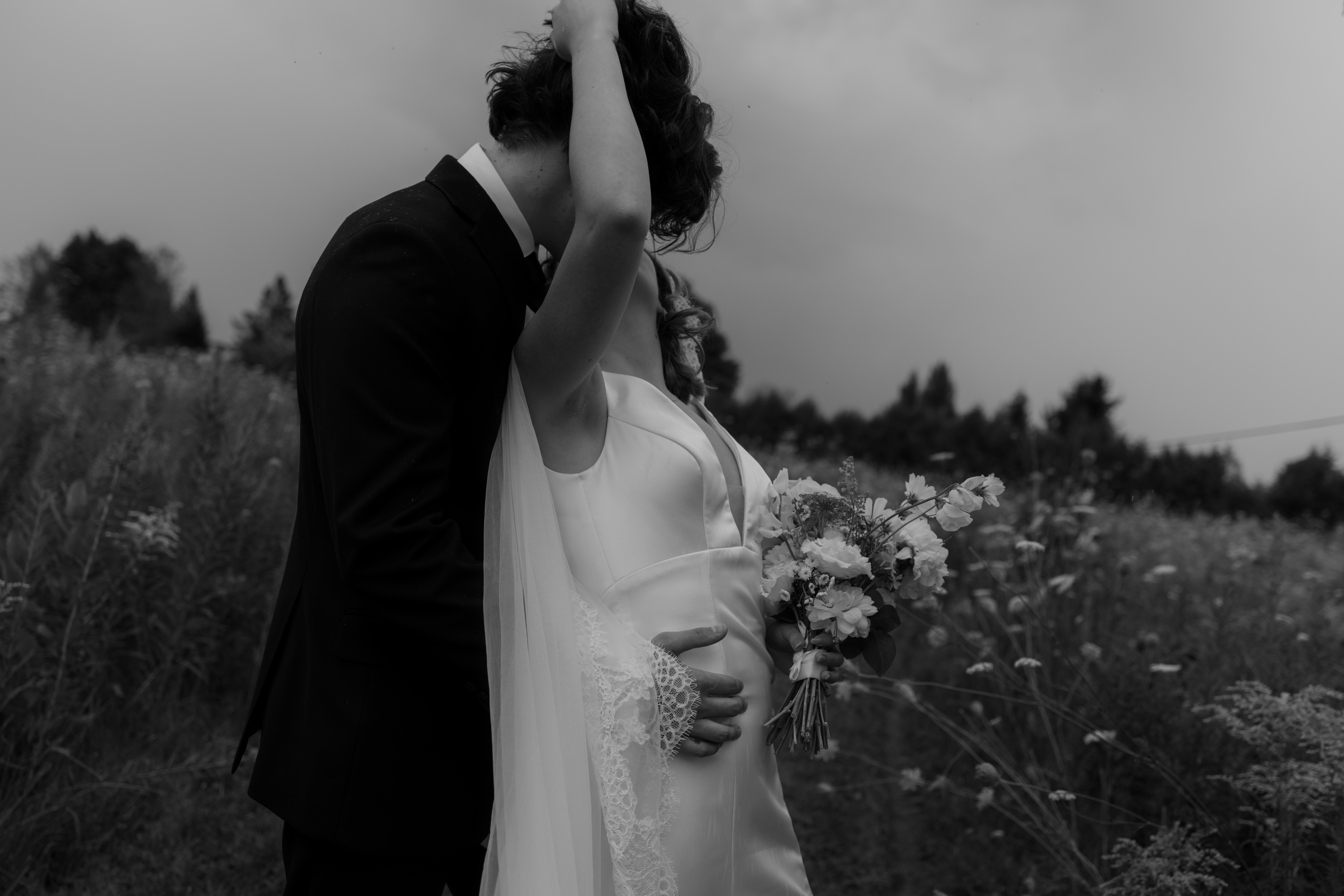 bride reaches back to give groom a kiss as he stands behind her 