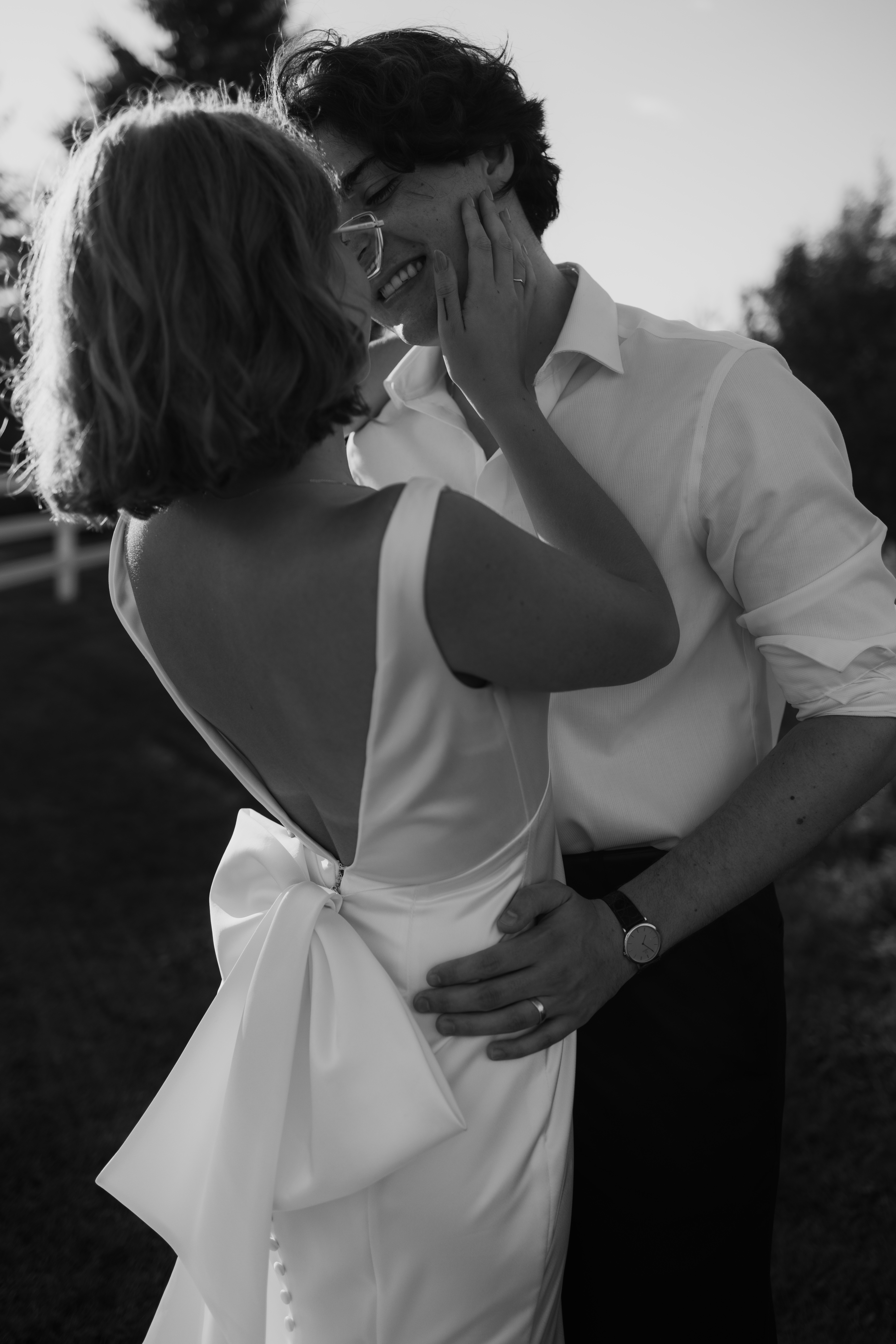 bride embraces grooms face as she wears sleek wedding gown with statement bow 