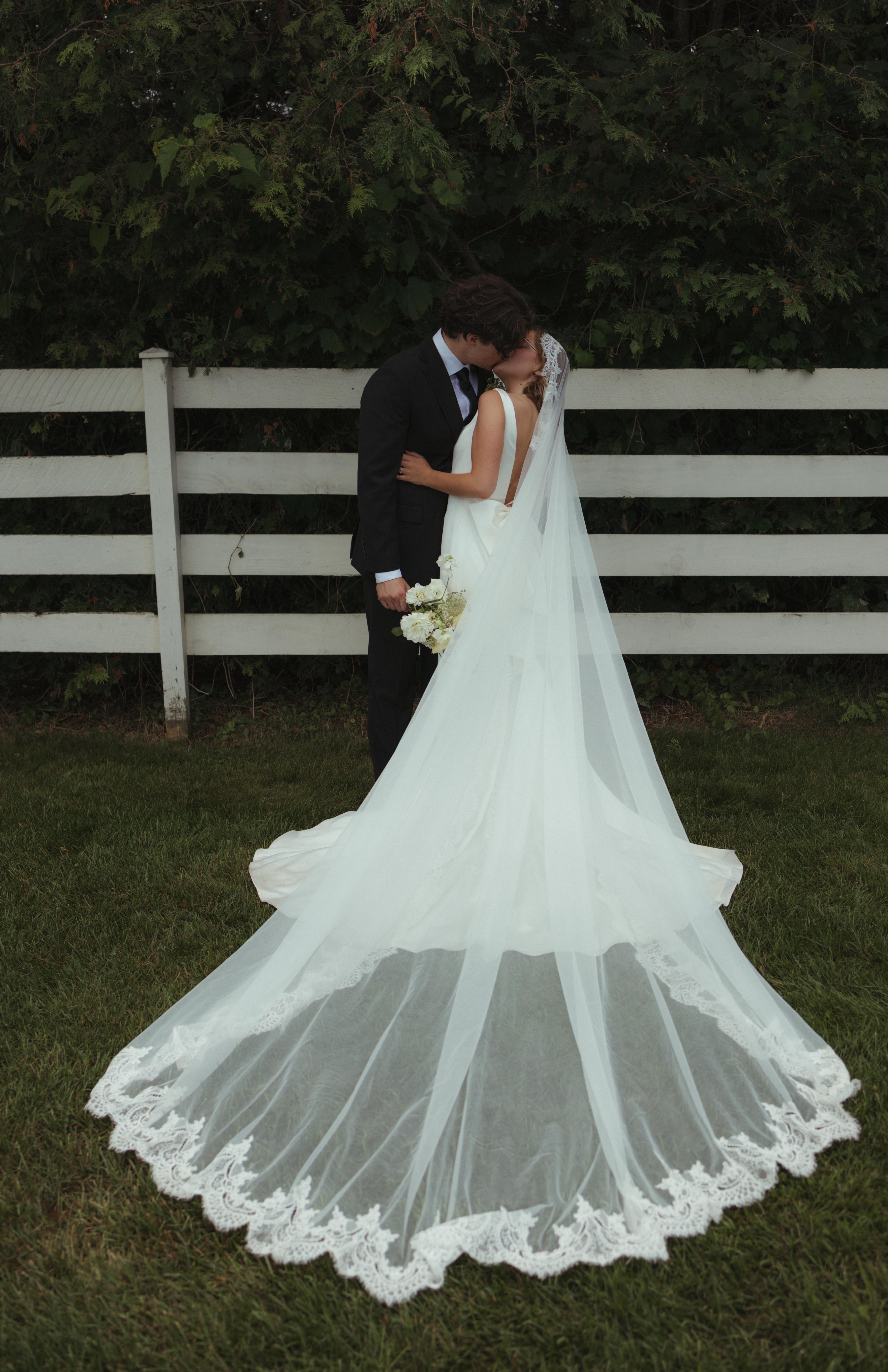 bride and groom kiss infront of white fence during portraits for their outdoor wedding ceremony
