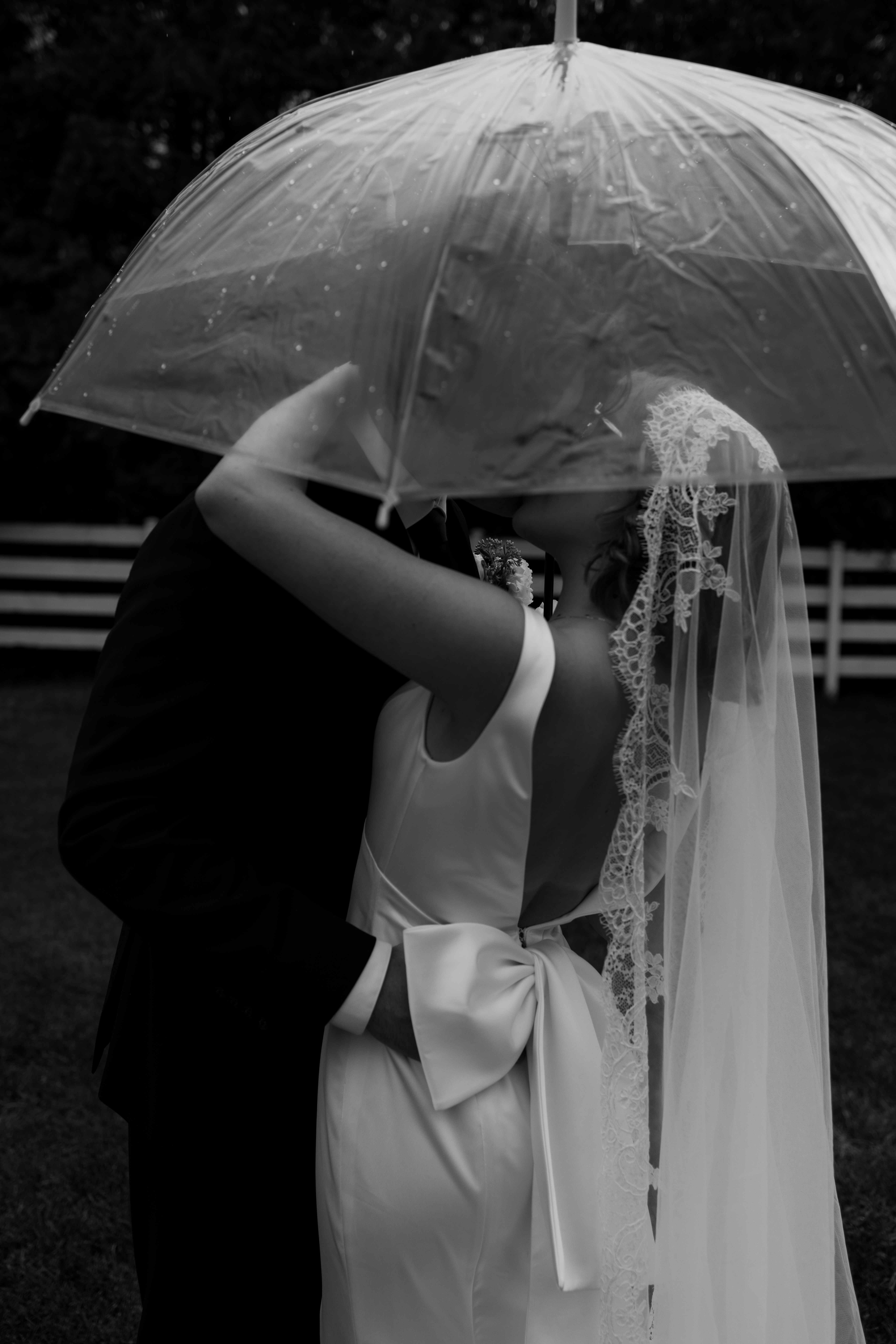 bride and groom kiss in the rain under umbrella 