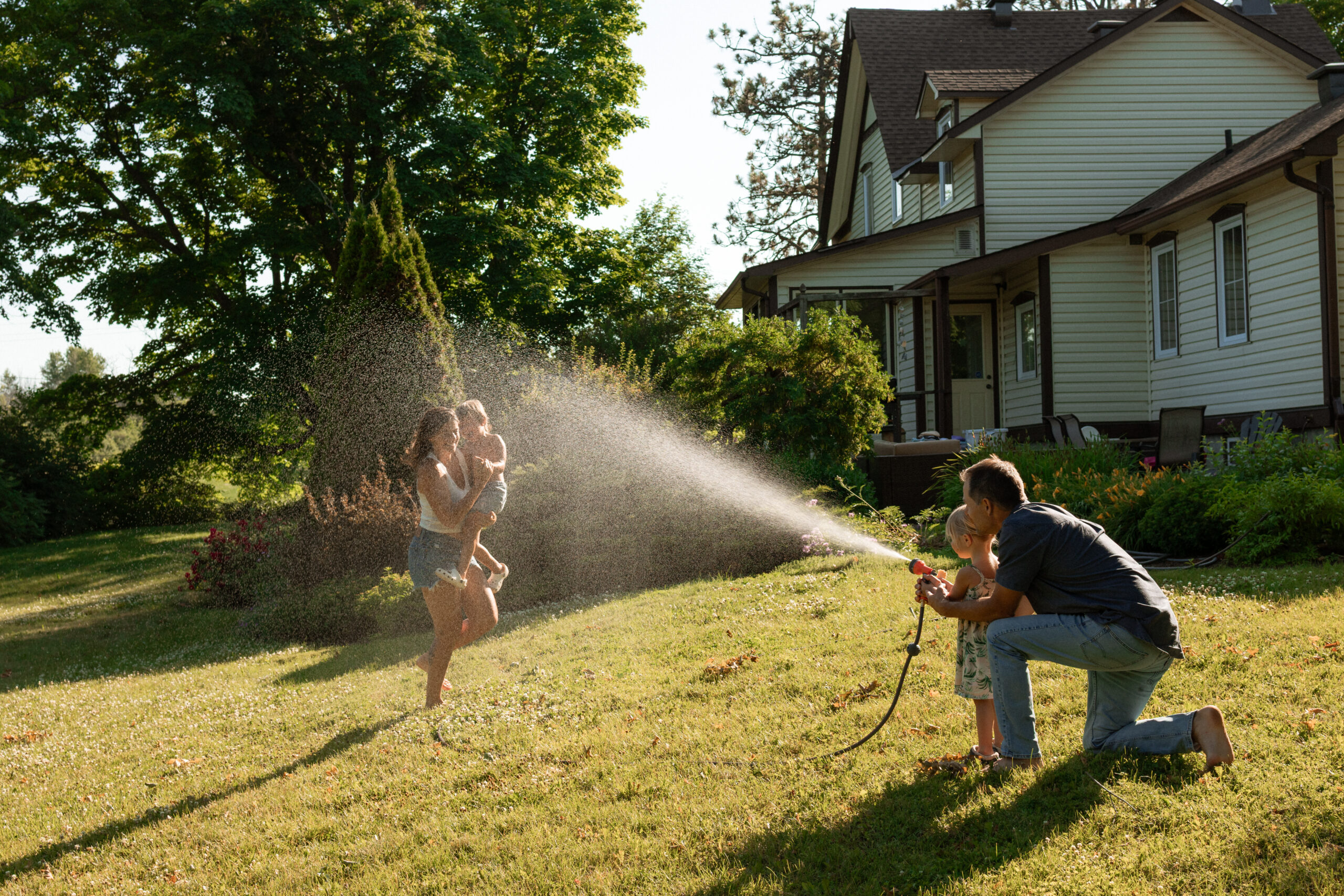 dad and daughter playing with the garden hose and mother and son run through it 